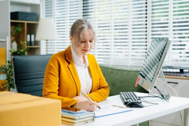 Startup small business SME, Entrepreneur owner woman using smartphone or tablet taking receive and checking online purchase shopping order to preparing pack product box. 