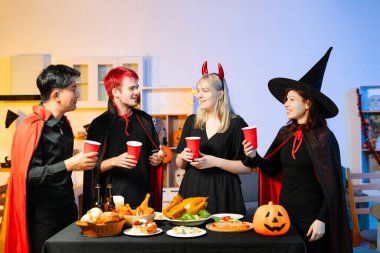 Cadılar Bayramı kostümlü arkadaşlar, balkabakları, kırmızı bardaklar ve kahkahalarla yapılan festival partisinde içkinin ve yemeğin tadını çıkarırlar. Mükemmel mevsimsel kutlama anı.