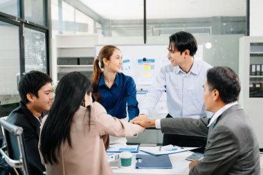 Gülümseyen Asyalı iş adamları başarılı bir toplantının ardından el ele tutuşuyorlar, takım çalışmasını, liderliği, motivasyonu ve şirket birliğini sembolize ediyorlar..