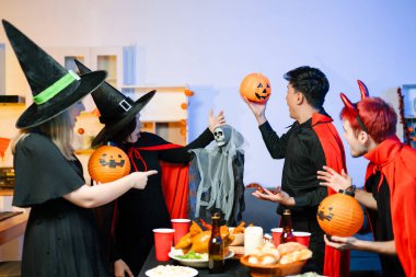 Cadılar Bayramı kostümlü bir grup arkadaş şenlikli bir partide ürkütücü aksesuar, fener ve kafatası dekoruyla gülüp oynuyorlar. Gerçek insanlar, yemek, içki ve neşe.