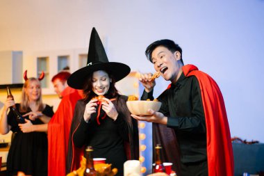 Neşeli ofis Cadılar Bayramı partisi kostüm giymiş iş arkadaşlarıyla, içkiler ve kahkahalarla kutlama, takım çalışmasını teşvik etme ve şenlik ruhu.