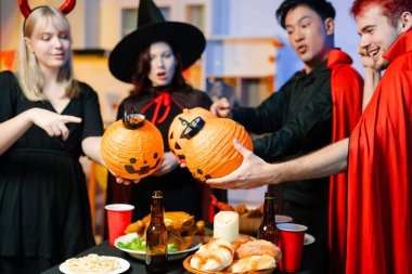 Cadılar Bayramı kostümlü bir grup arkadaş şenlikli bir partide ürkütücü aksesuar, fener ve kafatası dekoruyla gülüp oynuyorlar. Gerçek insanlar, yemek, içki ve neşe.
