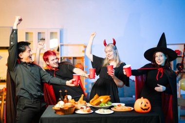 Cadılar Bayramı kostümlü arkadaşlar, balkabakları, kırmızı bardaklar ve kahkahalarla yapılan festival partisinde içkinin ve yemeğin tadını çıkarırlar. Mükemmel mevsimsel kutlama anı.