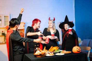 Cadılar Bayramı kostümlü arkadaşlar, balkabakları, kırmızı bardaklar ve kahkahalarla yapılan festival partisinde içkinin ve yemeğin tadını çıkarırlar. Mükemmel mevsimsel kutlama anı.