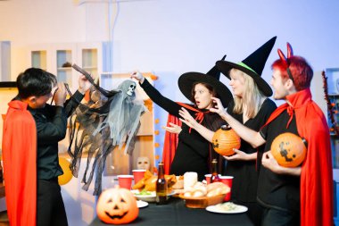 Neşeli ofis Cadılar Bayramı partisi kostüm giymiş iş arkadaşlarıyla, içkiler ve kahkahalarla kutlama, takım çalışmasını teşvik etme ve şenlik ruhu.