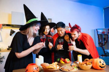 Cadılar Bayramı kostümleri kapalı bir partide kırmızı şarapla kadeh kaldırılır. Balkabakları, yemek ve kutlamalar eğlence, ürkütücü titreşimler ve mevsimlik neşe için ortam oluşturur..