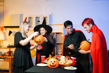 Neşeli ofis Cadılar Bayramı partisi kostüm giymiş iş arkadaşlarıyla, içkiler ve kahkahalarla kutlama, takım çalışmasını teşvik etme ve şenlik ruhu.