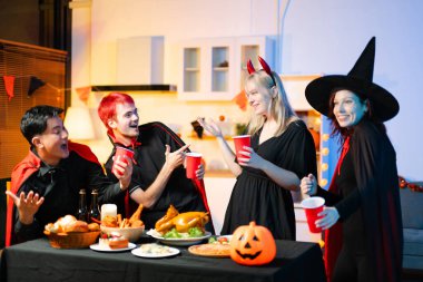 Cadılar Bayramı kostümlü arkadaşlar, balkabakları, kırmızı bardaklar ve kahkahalarla yapılan festival partisinde içkinin ve yemeğin tadını çıkarırlar. Mükemmel mevsimsel kutlama anı.