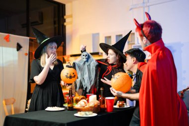 Cadılar Bayramı kostümlü bir grup arkadaş şenlikli bir partide ürkütücü aksesuar, fener ve kafatası dekoruyla gülüp oynuyorlar. Gerçek insanlar, yemek, içki ve neşe.