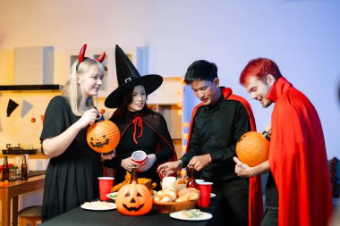 Cadılar Bayramı kostümlü genç arkadaşlar kapalı bir partide balkabağı feneri süslüyorlar. Gerçek insanlar ürkütücü titreşimleri, kırmızı bardakları, atıştırmalıkları ve Cadılar Bayramı aksesuarlarını severler..