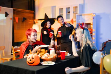 Neşeli ofis Cadılar Bayramı partisi kostüm giymiş iş arkadaşlarıyla, içkiler ve kahkahalarla kutlama, takım çalışmasını teşvik etme ve şenlik ruhu.