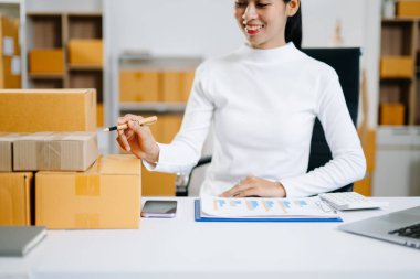 Genç işyeri sahibi kadın paket kutusunu hazırla ve tablet, dizüstü bilgisayar alışverişi online konsept üzerinden müşteriye teslimat için çevrimiçi kontrol yap.