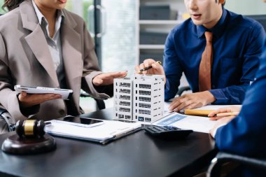 Profesyonel ekip, modern bir ofiste emlak modelleri ve bir tokmak ile iş görüşmeleri ve emlak geliştirme temalarının altını çizen bir hukuk sözleşmesini tartışıyor.