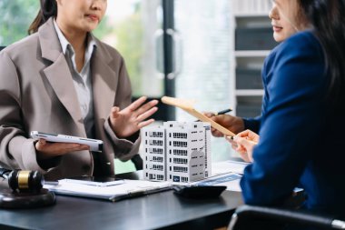 Profesyonel ekip, modern bir ofiste emlak modelleri ve bir tokmak ile iş görüşmeleri ve emlak geliştirme temalarının altını çizen bir hukuk sözleşmesini tartışıyor.