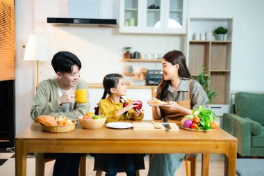 Kızıyla gülümseyen Asyalı aile modern bir mutfakta meyve ve sebze hazırlıyor. Sağlıklı beslenme, ebeveynlik, bağlılık ve evde aile zamanı kavramı.