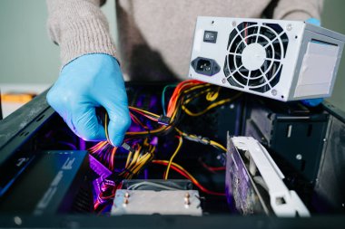 Masaüstü bilgisayar montajı sırasında güç kaynağı ve kablolarıyla ilgilenen eldiven teknisyeni. Bilgisayar onarımı, PSU kurulumu ve donanım güvenliği gibi konular için mükemmel.