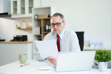 Modern ofis masasında dizüstü bilgisayarlı ve kahveli basılı belgeleri analiz eden, iş stratejisi, finans veya kurumsal kararlar üzerinde çalışan üst düzey yönetici..