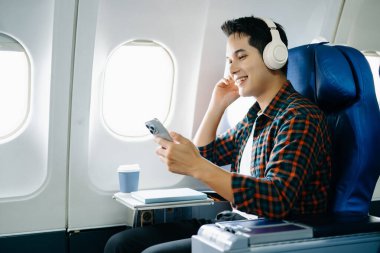 Uçak koltuğunda mutlu bir adam. Çeşitli seyahat dizileri: uzun bir uçuşta iş, konuşma, arama, dinleme, okuma, stres ve keyif. Teknoloji, cep telefonu ve görüntü yolculuğun anahtar kısımları..