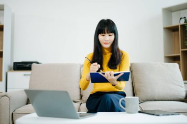 Genç bir kadın akıllı telefon kullanarak kanepede dinleniyor ve çevrimiçi cep telefonuna bakarken gülümsüyor, internette mesajlaşıyor, evdeki kanepede online alışveriş yapıyor.