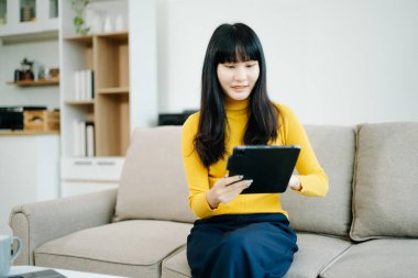 Genç bir kadın akıllı telefon kullanarak kanepede dinleniyor ve gülümsüyor. İnternette gezinirken cep telefonu kullanıyor, internette mesajlaşıyor, evdeki kanepede online alışveriş yapıyor.