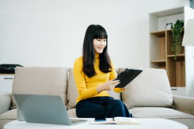 Genç bir kadın akıllı telefon kullanarak kanepede dinleniyor ve çevrimiçi cep telefonuna bakarken gülümsüyor, internette mesajlaşıyor, evdeki kanepede online alışveriş yapıyor.