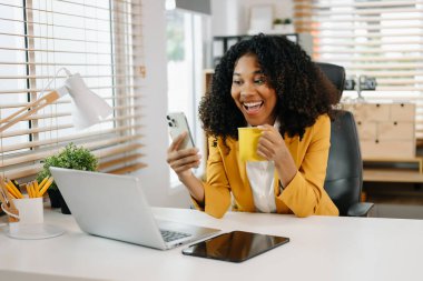 Genç, güzel bir kadın, modern ofisteki çalışan beyaz masada otururken tablet ve dizüstü bilgisayarda yazı yazıyor.