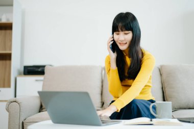 Genç bir kadın akıllı telefon kullanarak kanepede dinleniyor ve gülümsüyor. İnternette gezinirken cep telefonu kullanıyor, internette mesajlaşıyor, evdeki kanepede online alışveriş yapıyor.