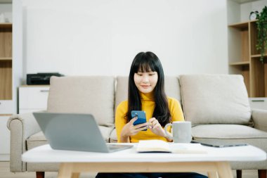 Genç bir kadın akıllı telefon kullanarak kanepede dinleniyor ve gülümsüyor. İnternette gezinirken cep telefonu kullanıyor, internette mesajlaşıyor, evdeki kanepede online alışveriş yapıyor.