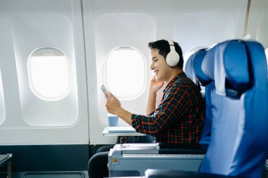 Uçak koltuğunda mutlu bir adam. Çeşitli seyahat dizileri: uzun bir uçuşta iş, konuşma, arama, dinleme, okuma, stres ve keyif. Teknoloji, cep telefonu ve görüntü yolculuğun anahtar kısımları..