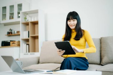 Genç bir kadın akıllı telefon kullanarak kanepede dinleniyor ve çevrimiçi cep telefonuna bakarken gülümsüyor, internette mesajlaşıyor, evdeki kanepede online alışveriş yapıyor.