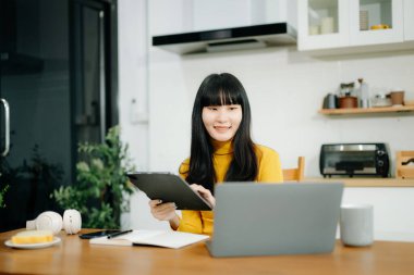 Samimi bir çalışma alanında dizüstü bilgisayarı ve tabletleri olan Asyalı genç bir kadının portresi. Mutfakta..