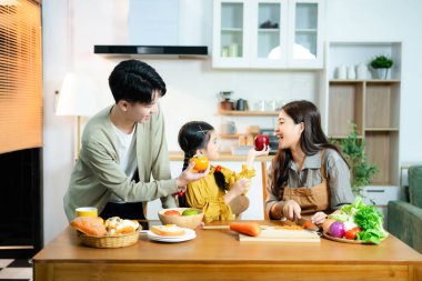 Kızıyla gülümseyen Asyalı aile modern bir mutfakta meyve ve sebze hazırlıyor. Sağlıklı beslenme, ebeveynlik, bağlılık ve evde aile zamanı kavramı.