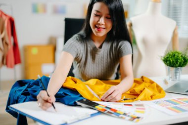 Asyalı moda tasarımcısı ev stüdyosundaki kumaşı manken ve dizüstü bilgisayarla ölçüyor. Yaratıcı moda işi, terzi planlaması