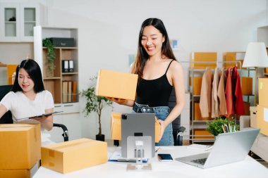 Startup small business SME, Entrepreneur owner woman using smartphone or tablet taking receive and checking online purchase shopping order to preparing pack product box.