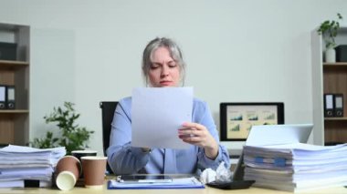 Masasında kağıt dokümanları inceleyen mavi gömlekli profesyonel sarışın kadın.