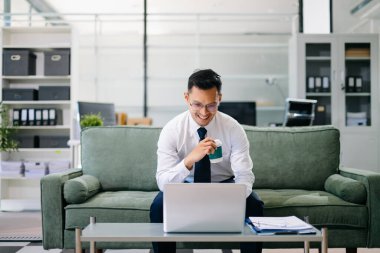 Modern bir ofiste tabletle çalışan Asyalı işadamı belgelere bakarken güvenle gülümsüyor..