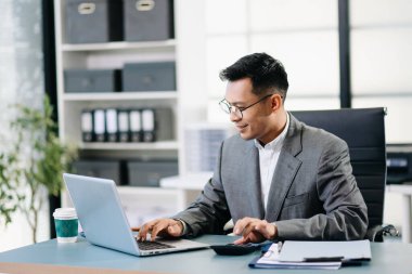 Asyalı adam çalıştığı yerde bilgisayarını ve tabletini kullanıyor. Ofisteki işine odaklan.