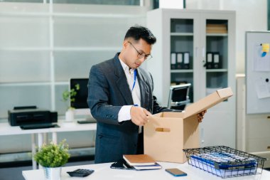 Hüzünlü işadamı işten çıkarılma üzerine kutu ve kimlik kartıyla ofiste oturuyor. İş kaybı ve iş stresi yüzünden kendini yorgun ve depresif hissediyor..