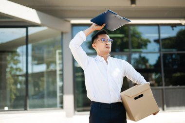 İşadamı kovulduktan sonra kutu ve dosya tutarken, modern şirket binasını terk ederken üzüntü ve belirsizlik gösteriyor..