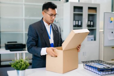 Hüzünlü işadamı işten çıkarılma üzerine kutu ve kimlik kartıyla ofiste oturuyor. İş kaybı ve iş stresi yüzünden kendini yorgun ve depresif hissediyor..