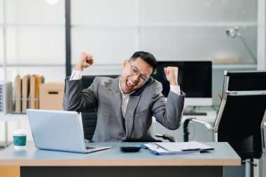 İş adamı, modern bir ofiste akıllı telefonuyla iyi haberler aldıktan sonra başarıyı kutluyor. Profesyonel bir iş ortamında sevinç ve başarıyı ifade ediyor..