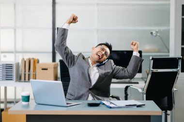 İş adamı, modern bir ofiste akıllı telefonuyla iyi haberler aldıktan sonra başarıyı kutluyor. Profesyonel bir iş ortamında sevinç ve başarıyı ifade ediyor..