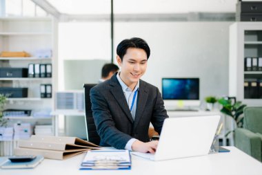 Zeki modern ofiste dizüstü bilgisayar ve pano üzerinde çalışan kendine güvenen Asyalı işadamı profesyonelliği, başarıyı ve takım çalışmasını simgeliyor..