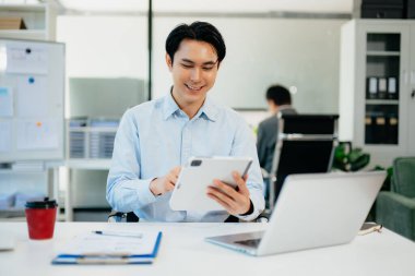 Asyalı adam çalıştığı yerde bilgisayarını ve tabletini kullanıyor. İşine odaklan..