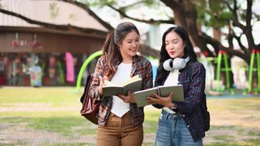 İki mutlu kız öğrenci parkta durmuş çalışmalarını tartışıyor ve kitap tutuyorlardı.