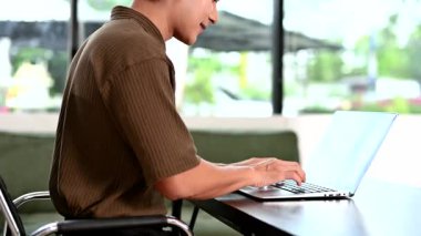 Parlak bir ofiste dizüstü bilgisayarda çalışan gülümseyen Asyalı adam.