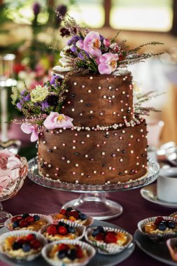 İki katlı düğün pastası bej rengi. El yapımı çikolata gülleri ve yapay çiçeklerle süslenmiş. İç kısımda fotoğraflar var. Sert ışık. Yakın plan..