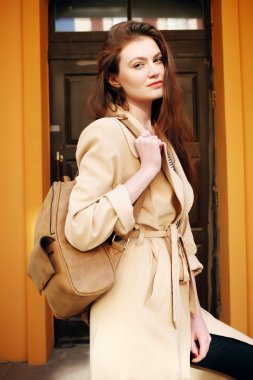Young stylish hipster girl wearing modern trench coat walking in urban city smiling happy. 