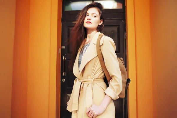 Joven chica hipster elegante con gabardina moderna caminando en la ciudad urbana sonriendo feliz . — Foto de Stock