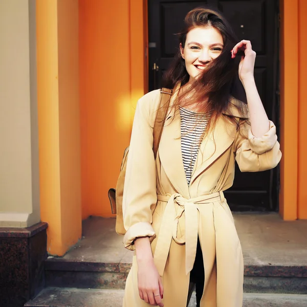 Joven chica hipster elegante con gabardina moderna caminando en la ciudad urbana sonriendo feliz . —  Fotos de Stock